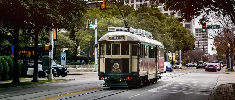 A trolley car slowly rolls down a tree-covered Dallas street