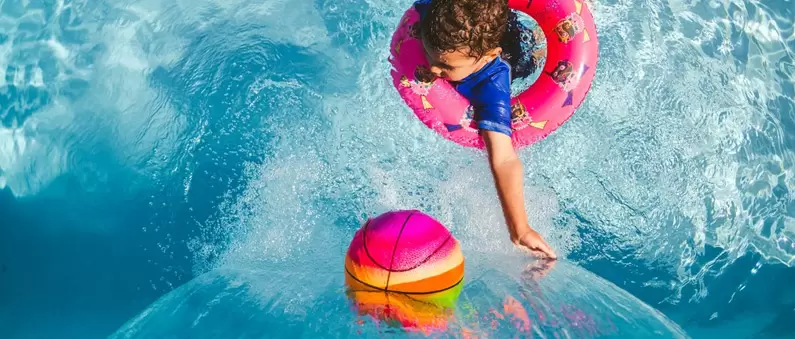 A young child in a floatie plays with a multi-colored ball at a East Dallas Fort Worth waterpark