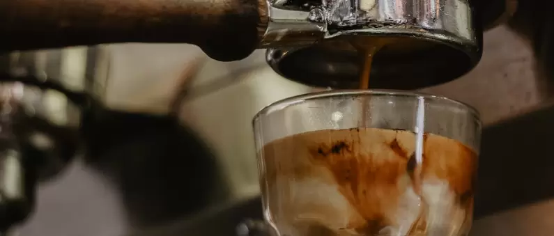 Espresso drips from an espresso machine into a glass of milk at a West Pittsburgh coffee shop